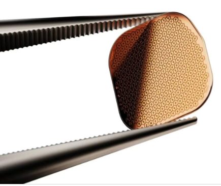 Chip do implante PRIMA seguro por uma pinça cirúrgica, mostrando a superfície formada por centenas de células fotovoltaicas hexagonais.